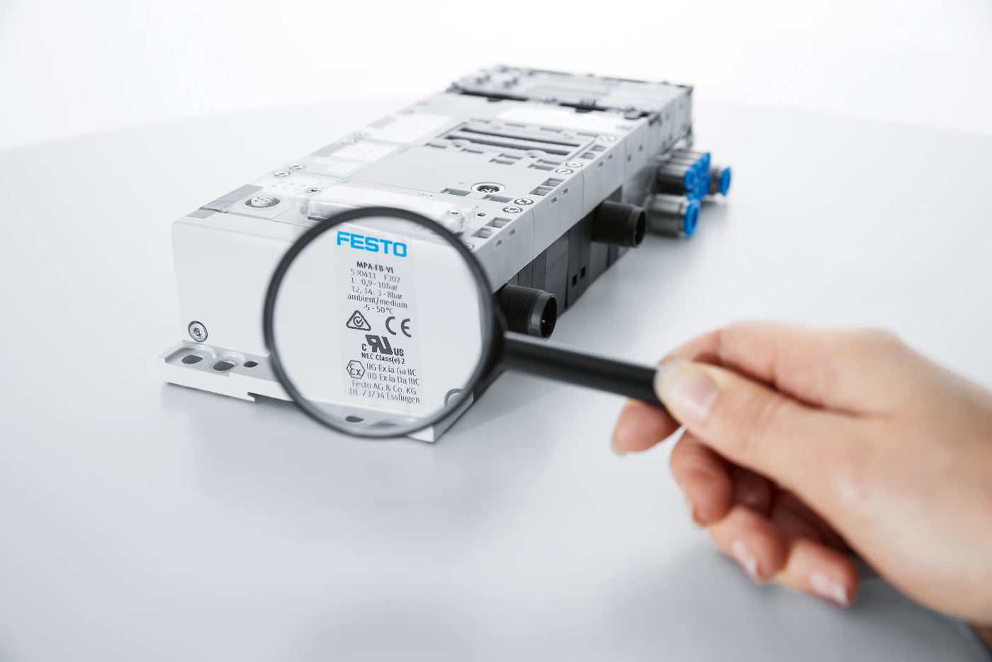 Person using a magnifying glass to inspect a Festo product on a white background